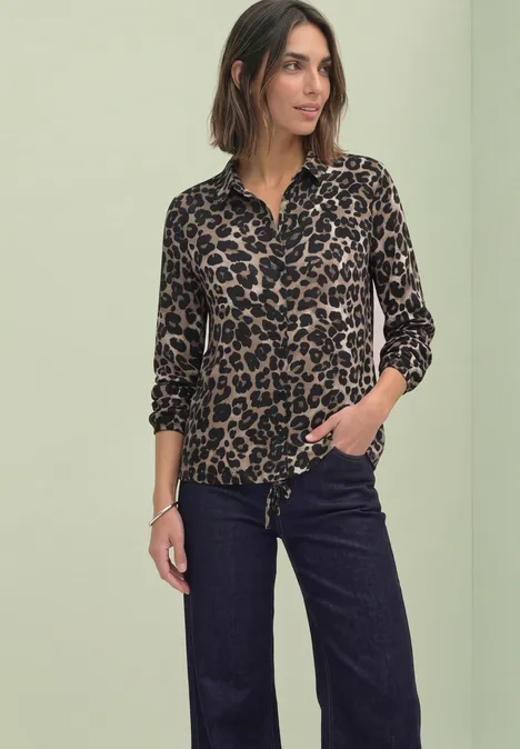 Langarm Shirt im Hemdblusen-Look Black Frau in Leopardenmuster-Bluse und dunklen Jeans vor grünem Hintergrund.