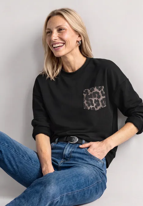 Fröhliche Frau in schwarzem Langarmshirt mit Leopardenmuster-Tasche und blauen Jeans.