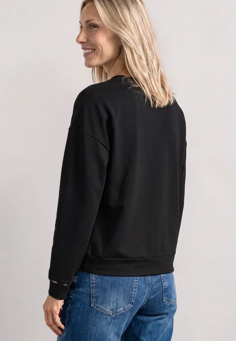Frau im Profil mit schwarzem Pullover und blauen Jeans.