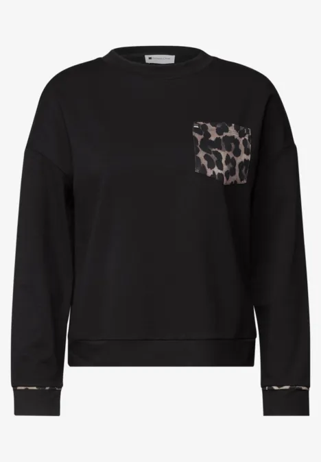 Schwarzer Sweatshirt mit Brusttasche im Leopardenprint und feinen Leo-Akzenten an Saum und Ärmeln.