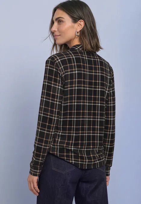 Femme porte chemise à carreaux manches longues et pantalon sombre, regarde par-dessus l'épaule.