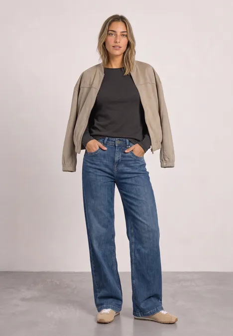 Frau in lässigem Outfit: schwarzes Shirt, beige Jacke, weite Jeans und passende Loafers.