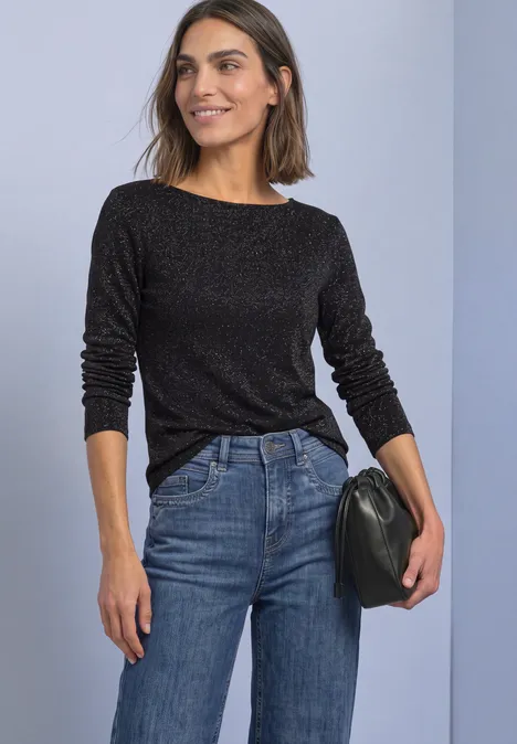 T-shirt à manches longues, col bateau et paillettes Black Frau trägt schwarzen Pullover, blaue Jeans und hält eine schwarze Clutch. Steht vor hellem Hintergrund.