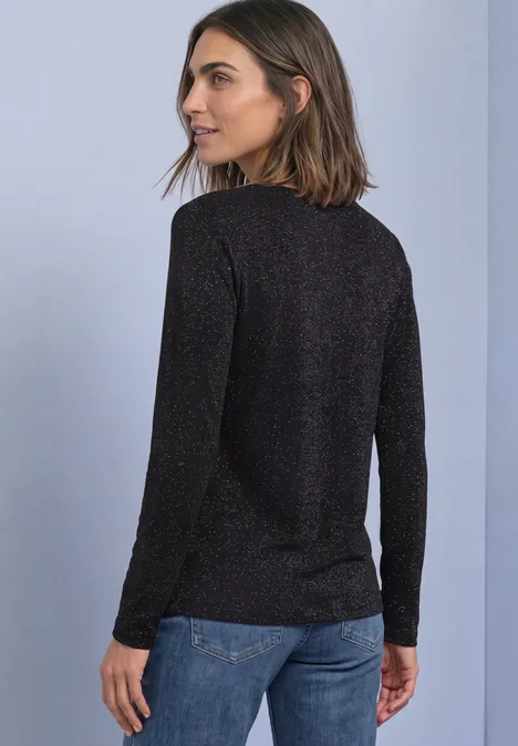 T-shirt à manches longues, col bateau et paillettes Black Frau im schwarzen Langarmpullover und Jeans steht mit dem Rücken zur Kamera und schaut über die Schulter.