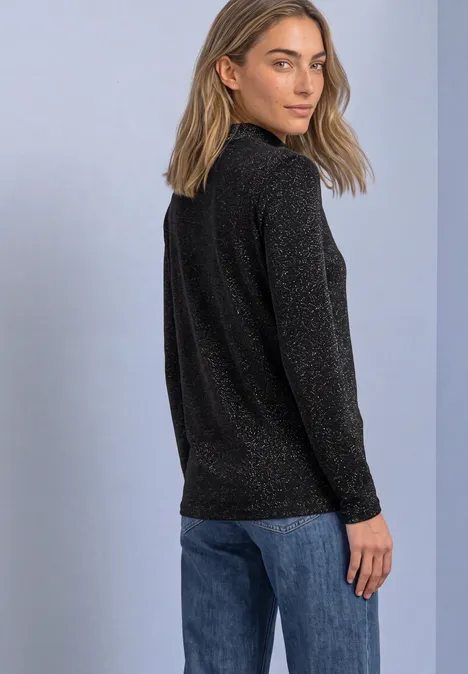 T-shirt à manches longues, col roulé et paillettes Black Frau in schwarzem Glitzerpullover und blauer Jeans blickt über die Schulter.