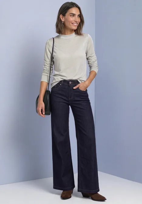 Frau trägt hellgrauen Pullover, hoch taillierte, weite Jeans, schwarze Umhängetasche und braune Schuhe.