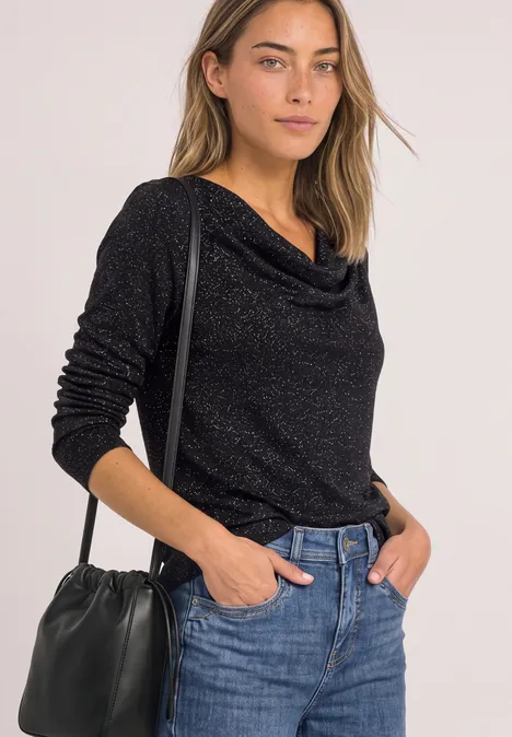 Vrouw in zwarte, langemouwen trui met watervalhals, blauwe jeans en zwarte schoudertas, halfportret.