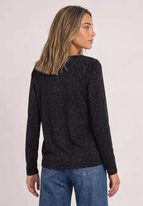Vrouw van achteren met zwarte glanzende top en blauwe spijkerbroek tegen lichte achtergrond.