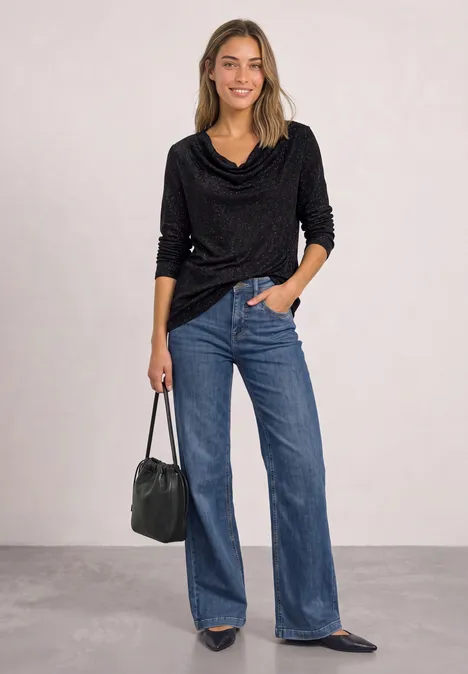 Vrouw in zwarte coltrui met watervalhals, wijde blauwe jeans, puntige flats en zwarte leren tas.