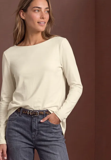 Een vrouw in een crèmekleurige longsleeve en jeans, casual pose.