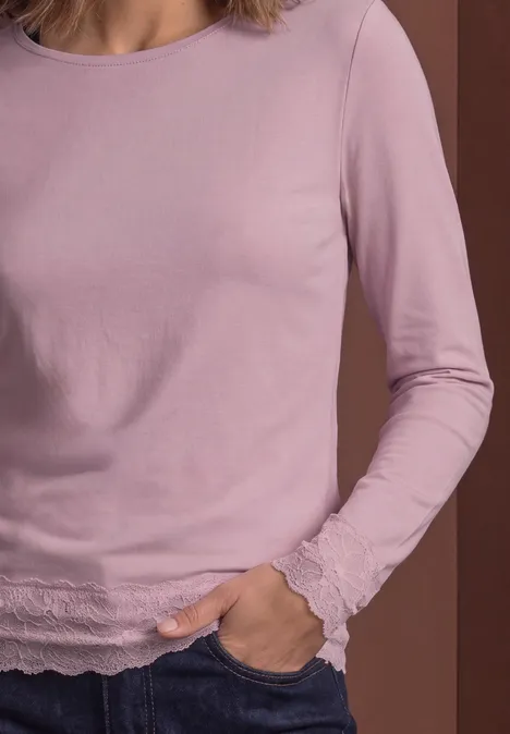 Vrouw draagt lichtpaars shirt met lange mouwen en kantafwerking, hand in de zak.