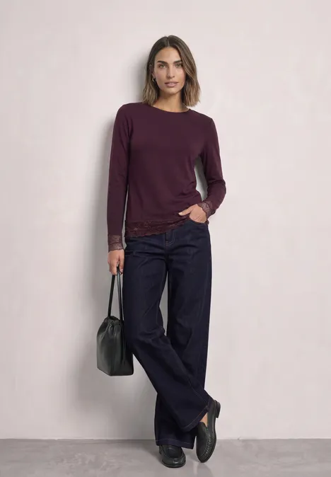 T-shirt à manches longues, col bateau et dentelle berry plum Eine Frau trägt einen bordeauxroten Pullover, weite dunkle Hosen und hält eine schwarze Tasche.