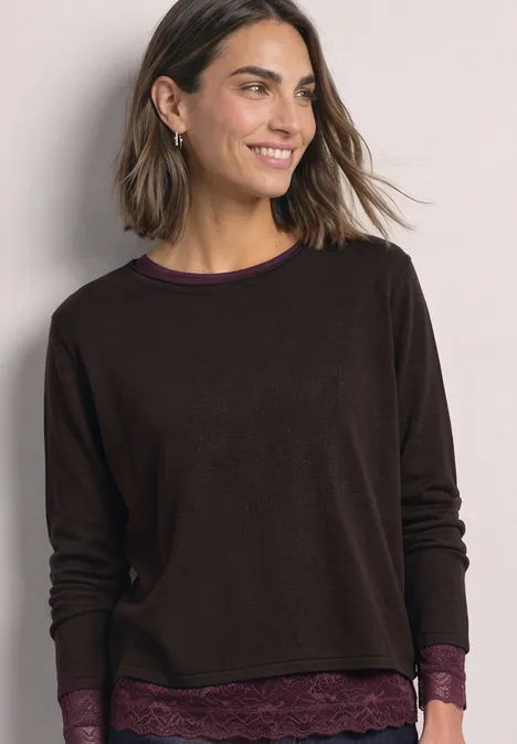 T-shirt à manches longues, col bateau et dentelle berry plum Frau trägt braunen Langarm-Pullover mit Spitzenbesatz, lächelt vor hellem Hintergrund.