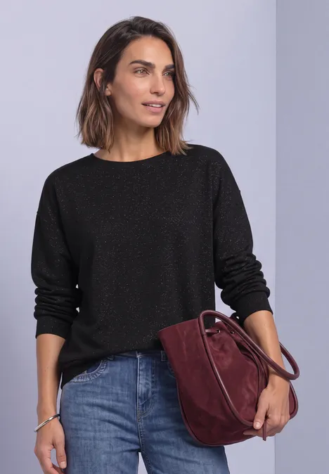 T-shirt en maille à manches chauve-souris Black Eine Frau trägt einen schwarzen Pullover, Jeans und eine dunkelrote Tasche vor hellem Hintergrund.