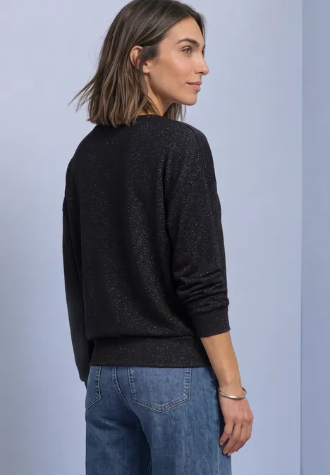 T-shirt en maille à manches chauve-souris Black Frau in schwarzem Pullover und Jeans, von der Seite stehend vor neutralem Hintergrund.