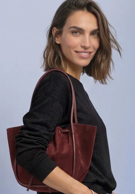 T-shirt en maille à manches chauve-souris Black Lächelnde Frau mit braunen Haaren trägt schwarzen Pullover und weinrote Tasche vor hellem Hintergrund.