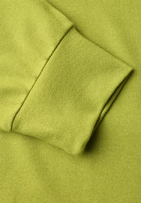 T-shirt en maille à manches chauve-souris apple lime Nahaufnahme eines grünen Sweatshirt-Ärmels mit Bündchen.