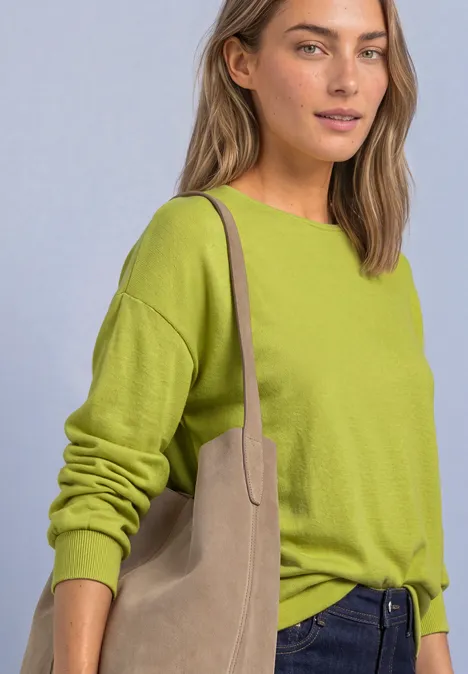 T-shirt en maille à manches chauve-souris apple lime Frau in limegrünem Pullover und Jeans trägt eine beigetöne Schultertasche vor hellem Hintergrund.
