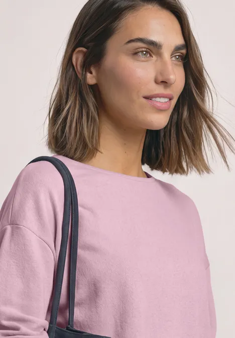 T-shirt en maille à manches chauve-souris quiet rose Eine junge Frau mit kurzen braunen Haaren, trägt ein rosa Shirt und eine Schultertasche.