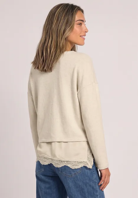 Frau in hellem Lagenpullover mit Spitzenbesatz trägt blaue Jeans, seitliche Ansicht.