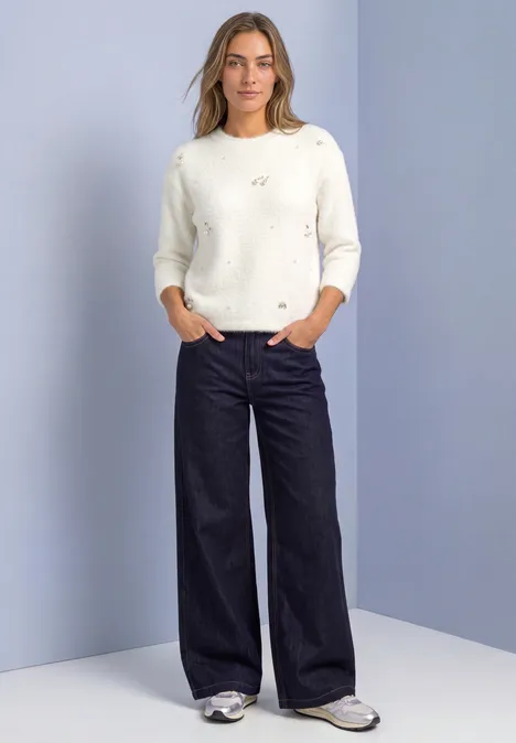 3/4-Arm Shirt mit dekorativen Details off white Frau in weißem Pullover und weiter, dunkler Hose, steht mit Händen in den Taschen.