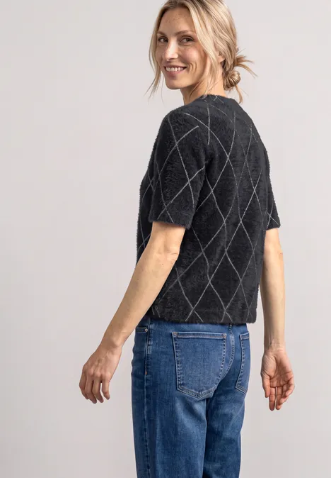 Pull à manches courtes et col rond à carreaux armor grey Une femme de profil souriante porte un pull court en maille noire à losanges et un jean bleu.