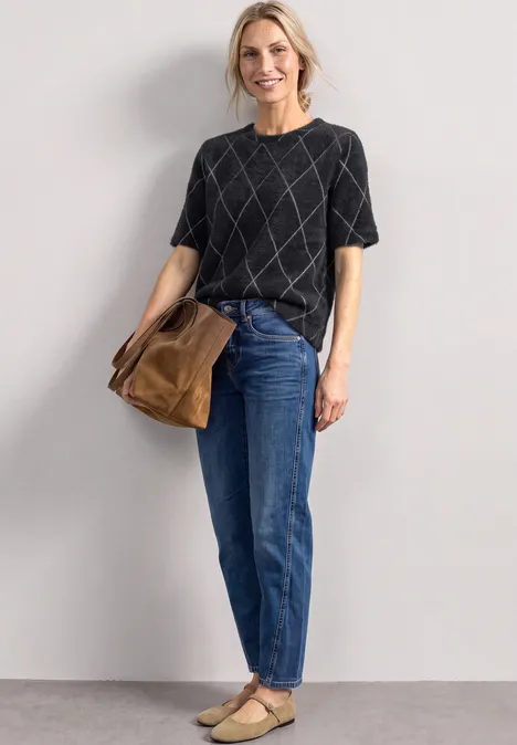 Pull à manches courtes et col rond à carreaux armor grey Une femme porte un T-shirt noir à motif losange, un jean bleu, des chaussures beiges et un sac marron.