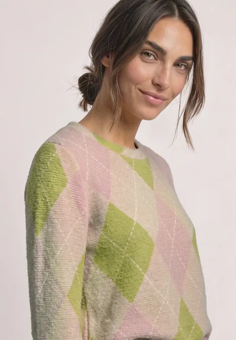 Frau mit braunen Haaren trägt Pullover mit Rautenmuster in Grün und Rosa.