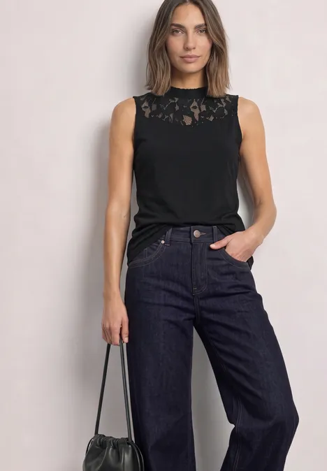 Top mit Rundhals und Spitze Black Eine Frau trägt ein ärmelloses Spitzen-Top in Schwarz, weite Jeans und hält eine schwarze Tasche.