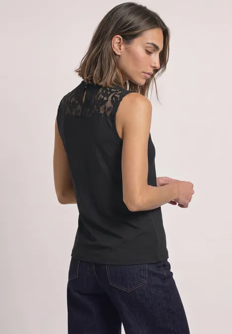 Top mit Rundhals und Spitze Black Frau von hinten in ärmellosem schwarzen Spitzen-Top und dunkler Jeans.