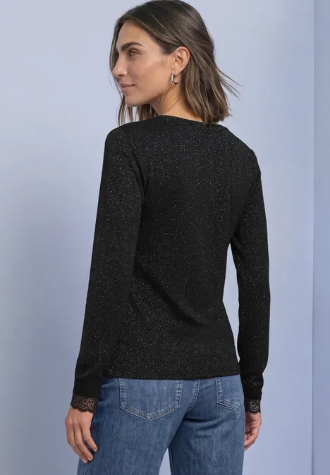 T-shirt à manches longues avec paillettes et dentelle Black Femme vue de dos portant un haut noir à manches longues scintillant et un jean bleu sur fond uni.