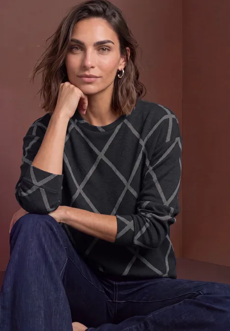 T-shirt à manches longues, col rond et motif à carreaux armor grey Femme portant un pull sombre à motifs géométriques, assise de manière décontractée devant un fond neutre.