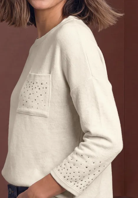 Beiger Pullover mit Brusttasche und Lochmuster auf Tasche und Ärmeln, seitliche Ansicht.
