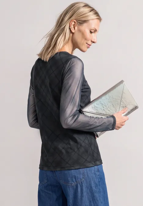 Frau mit blonden Haaren in schwarzem, transparentem Rautentop und Jeansrock hält beige Clutch.