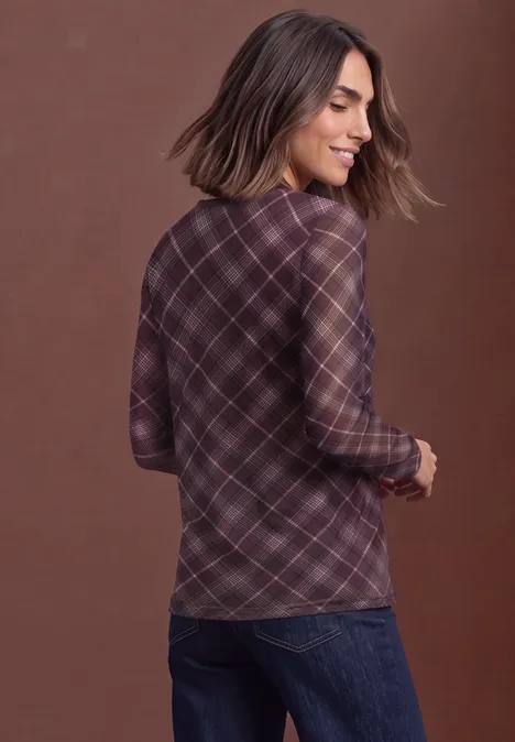 Vrouw van achteren in paarse geruite blouse en jeans, glimlachend zijwaarts kijkend.