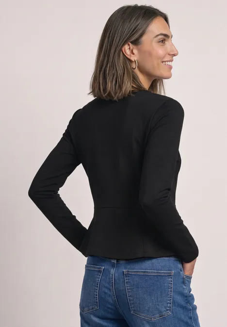 Frau trägt schwarzen, taillierten Blazer mit langen Ärmeln, steht seitlich abgewandt und lächelt.