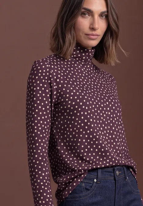 Frau in langärmligem Rollkragenshirt mit weißen Herzen und Jeans, braune schulterlange Haare.