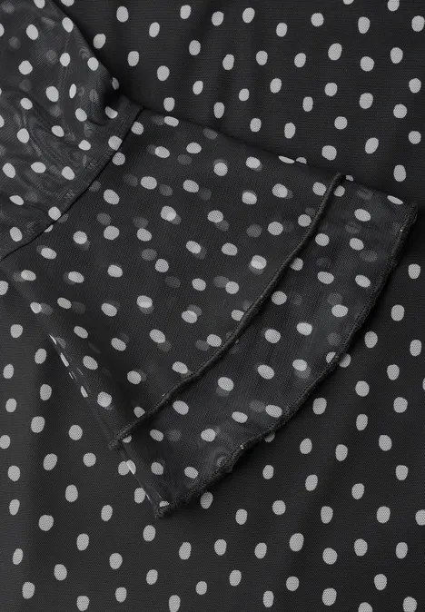 Schwarzer Stoff mit weißen Polka Dots und Rüschen am Ärmel.