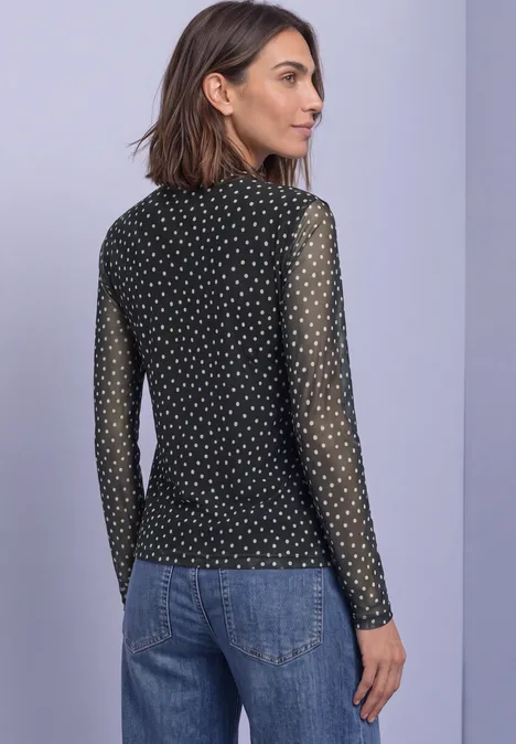 Frau im Profil mit schwarzem, gepunktetem Mesh-Langarmshirt und blauer Jeans.