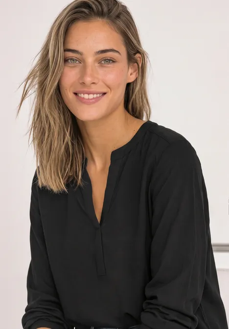 Split Neck Tunika Black Junge Frau mit langem Haar in schwarzer Bluse lächelt entspannt in die Kamera.