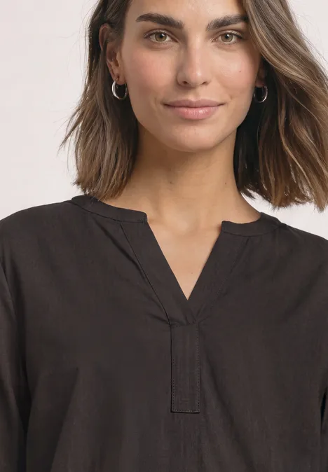 Split Neck Tunika black coffee Frau mit braunen Haaren trägt dunkelbraune Bluse mit V-Ausschnitt und silbernen Ohrringen, leichtes Lächeln.