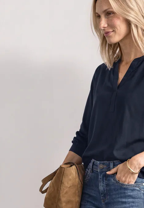 Frau in dunkelblauem Oberteil und Jeans, mit hellbrauner Tasche seitlich
