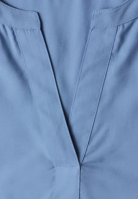 Lichtblauwe V-hals van stof, doet denken aan een medische tuniek of werkkleding.