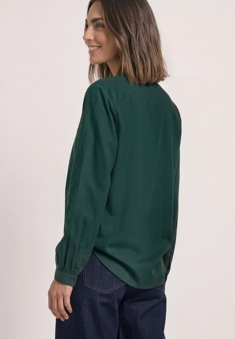 Tuniek met V-hals shadow teal Frau in dunkelgrüner Bluse und Jeans, seitlich stehend und lächelnd.