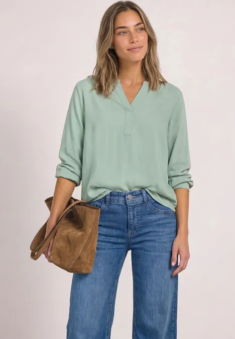 Frau in mintgrüner Bluse und Jeans, hält eine braune Tasche