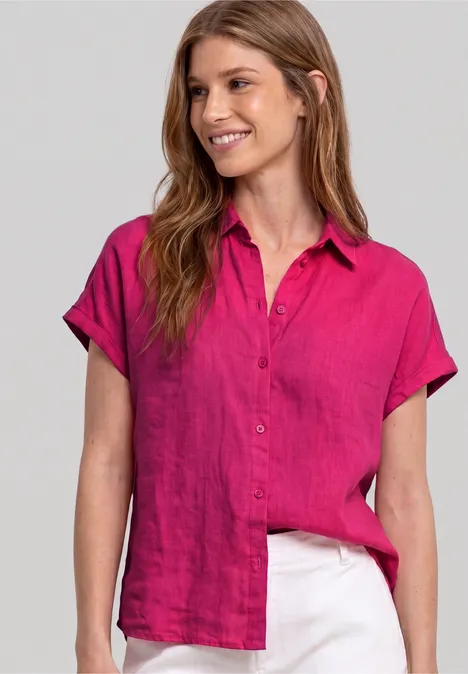 Vrouw in roze korte mouwen blouse en witte broek voor een grijze achtergrond.