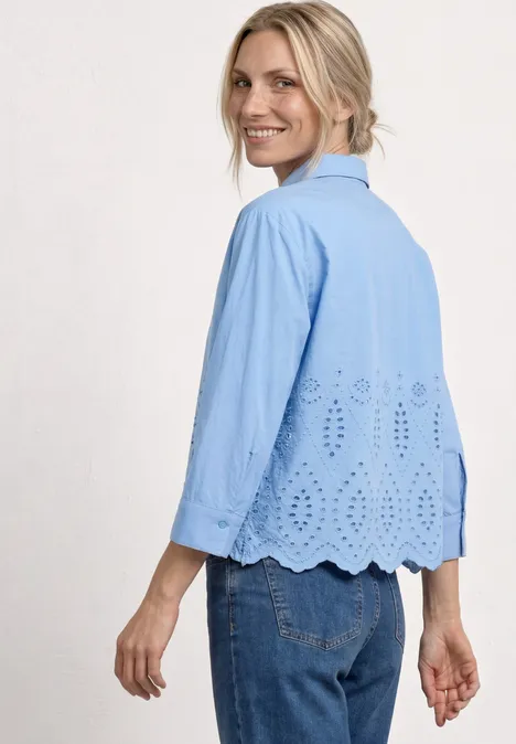 Vrouw in blauwe blouse met ajourpatroon en geschulpte zoom, van opzij gefotografeerd, gecombineerd met spijkerbroek.