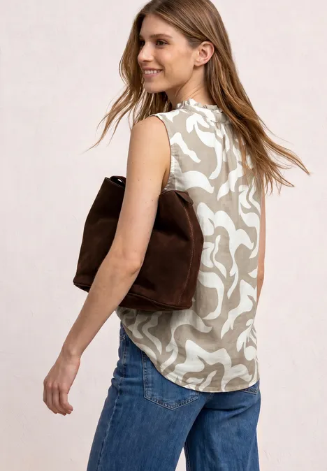 Vrouw in zijaanzicht met een beige top met bloemmotief, blauwe jeans en een bruine suède tas over de schouder.