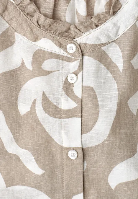 Close-up van een beige-witte blouse met bloemmotief en witte knopen.