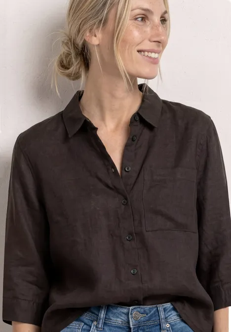 Frau in dunkelbraunem Leinenhemd mit 3/4-Ärmeln und Jeans vor hellem Hintergrund.